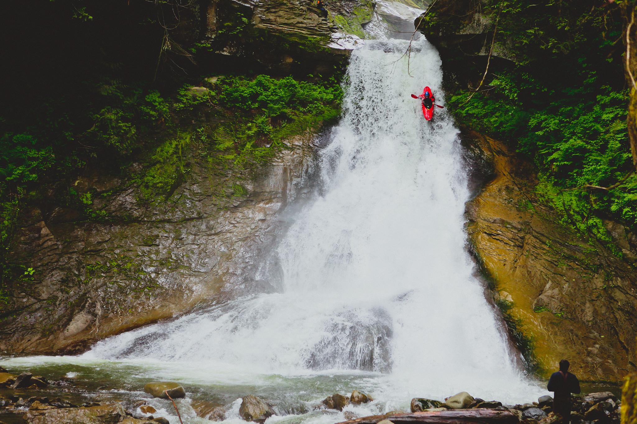 An orange kayak is paddling straight down a waterfall or very steep river. 