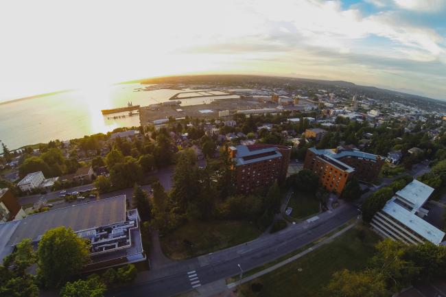 An aerial view of Bellingham at sunset. Some of the visible buildings are part of Western's campus, and many are not. Bellingham Bay and the waterfront are visible in the background.
