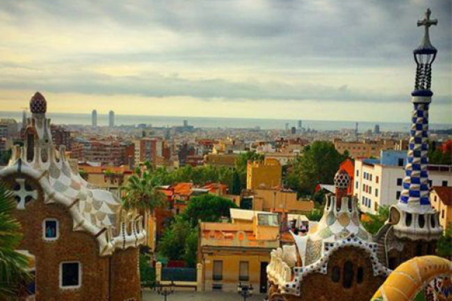Parque Güell in Barcelona, Spain. The famous La Sagrada Familia  Varied and colorful buildings fill the photo, some with spires that tower over the rest of the city. 
