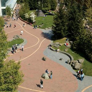 An image taken from a drone, looking down onto students walking along the wide paths between some of WWU's campus buildings. Some students are standing in groups, some sitting on benches along the path, and others are presumably walking to their next class.